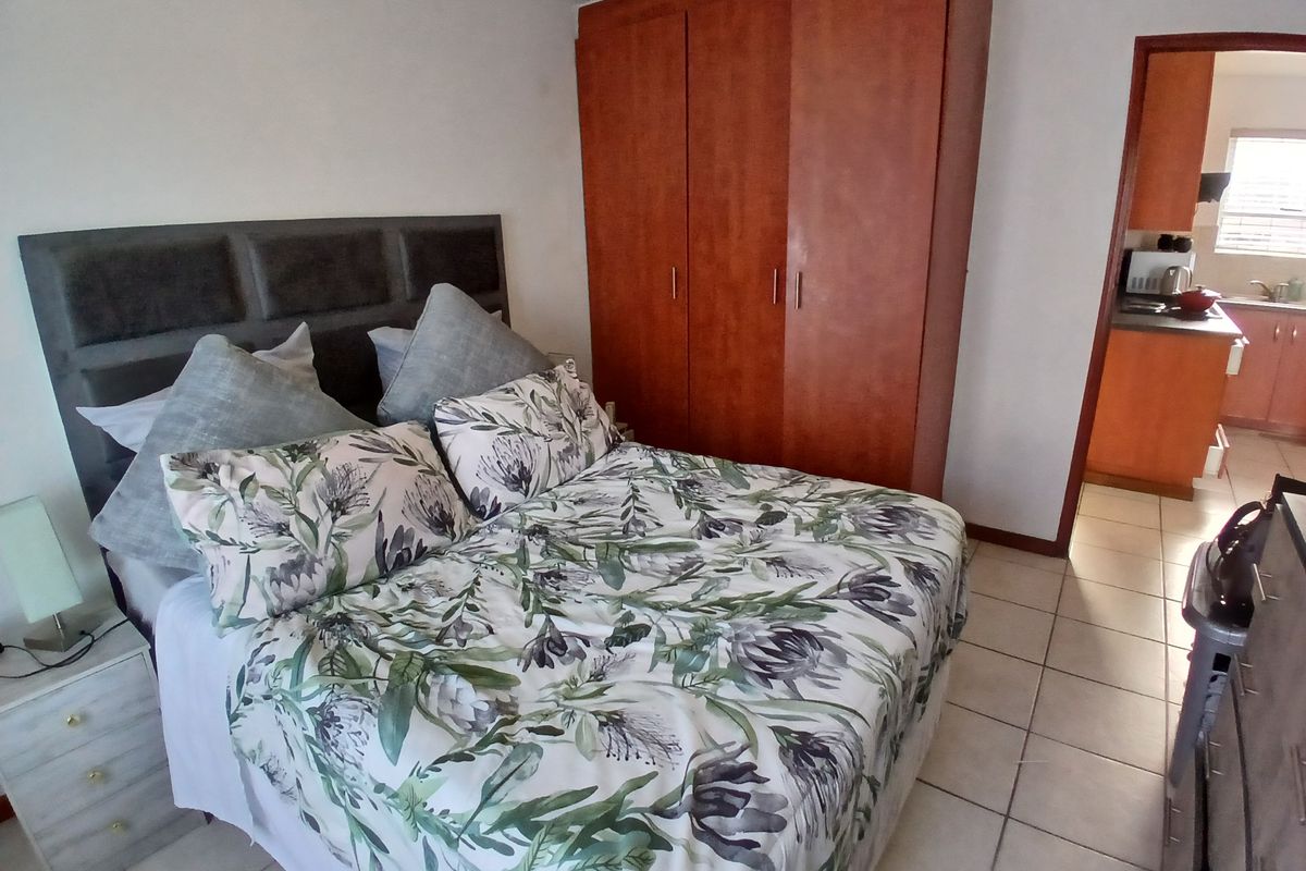 A bedroom featuring tiled flooring and a built-in wooden wardrobe, with a view into the adjacent kitchen area.