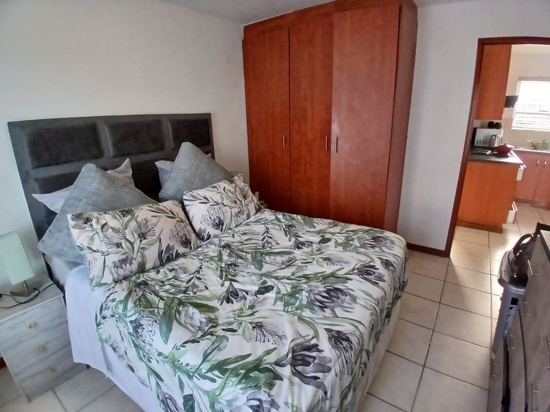 A bedroom featuring tiled flooring and a built-in wooden wardrobe, with a view into the adjacent kitchen area.