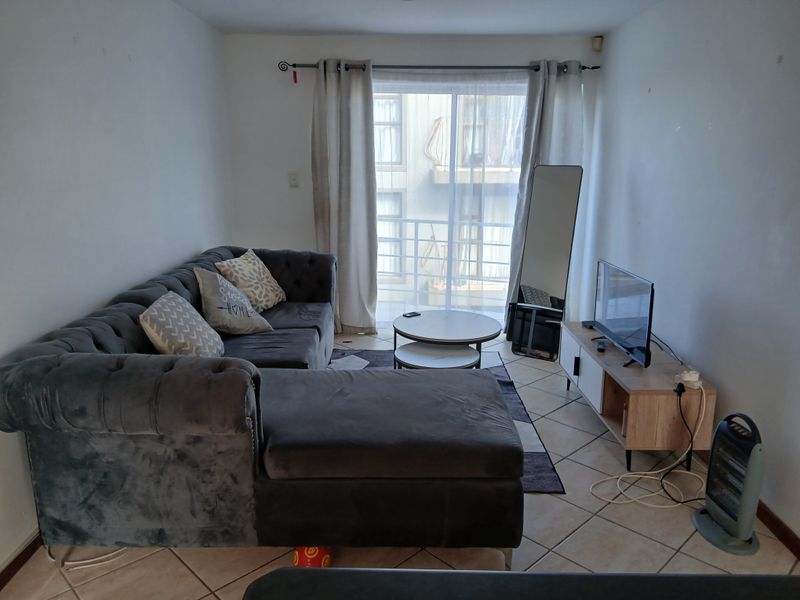 A living room featuring ceramic floor tiles and a sliding glass door leading to a balcony, providing natural light to the space.