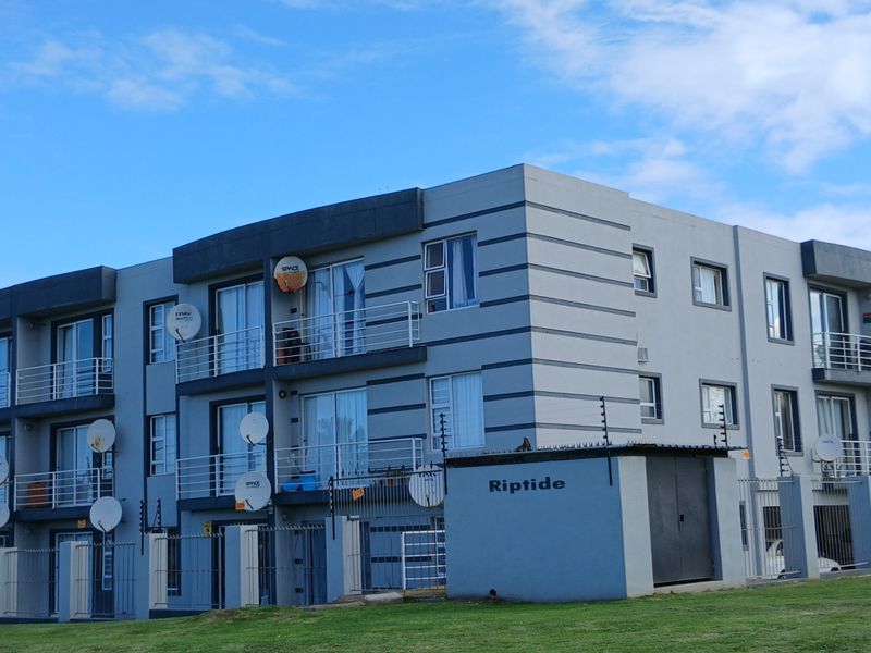 Exterior view of the Riptide apartment complex featuring multi-story units with private balconies, sliding doors, and perimeter security fencing.
