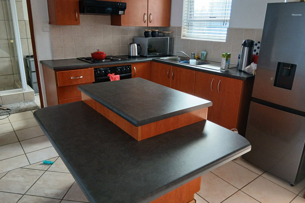 Functional kitchen featuring wood-tone cabinetry, dark laminate countertops, a central island, and tiled flooring, offering a practical layout for daily meal preparation.