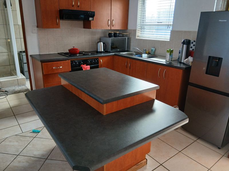 Functional kitchen featuring wood-tone cabinetry, dark laminate countertops, a central island, and tiled flooring, offering a practical layout for daily meal preparation.