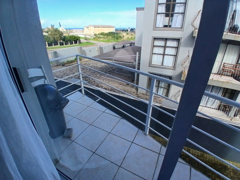 A functional balcony featuring tiled flooring and a metal balustrade, offering an elevated view of the surrounding apartment complex and neighborhood.