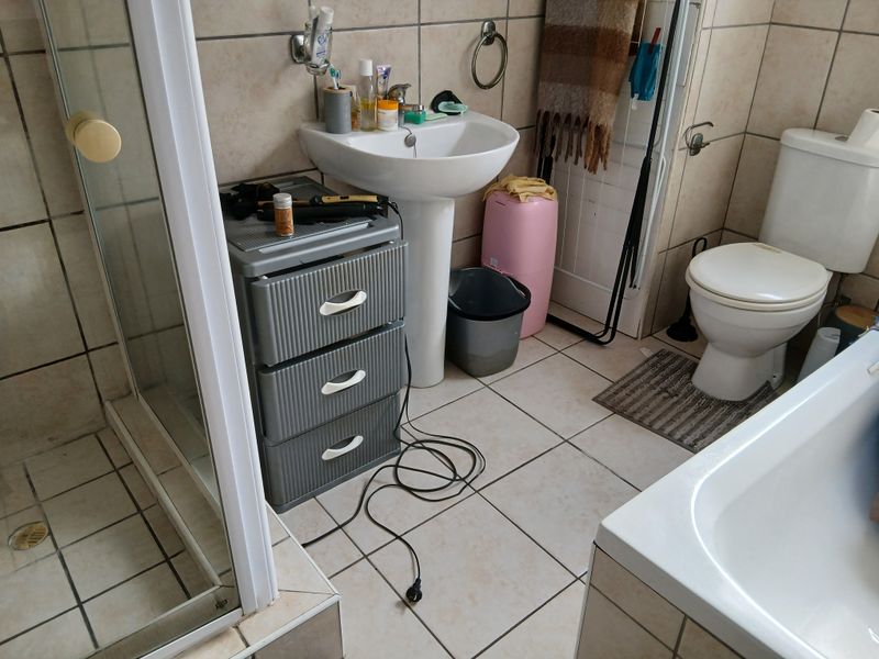 A functional bathroom featuring a pedestal washbasin, shower enclosure, bathtub, and toilet with neutral wall and floor tiling.