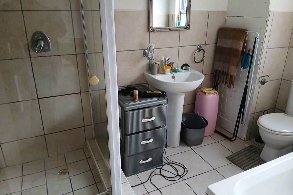 A functional bathroom featuring a shower enclosure, pedestal basin, and toilet with tiled finishes, requiring some maintenance and cosmetic updates.