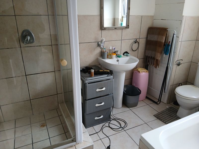 A functional bathroom featuring a shower enclosure, pedestal basin, and toilet with tiled finishes, requiring some maintenance and cosmetic updates.