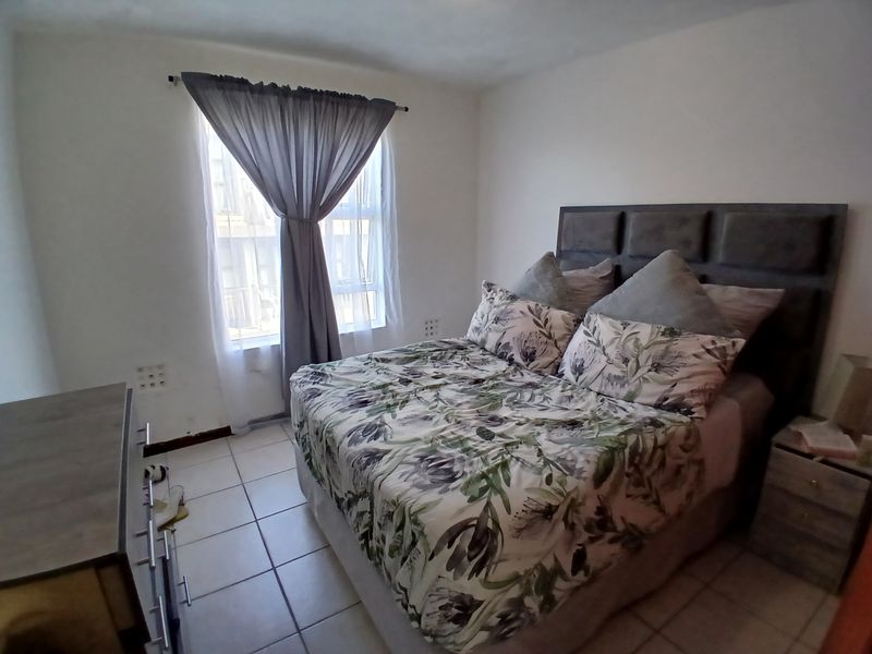A functional bedroom featuring tiled flooring and a window with curtains, providing a simple and practical living space.