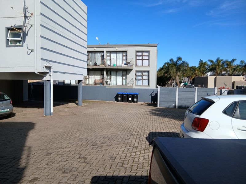 Rear exterior view of the apartment complex featuring a paved parking area, boundary wall, and residential balconies.