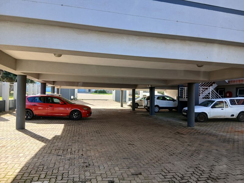 A covered ground-level parking area featuring concrete support pillars and paved flooring, providing sheltered vehicle storage for the apartment complex.