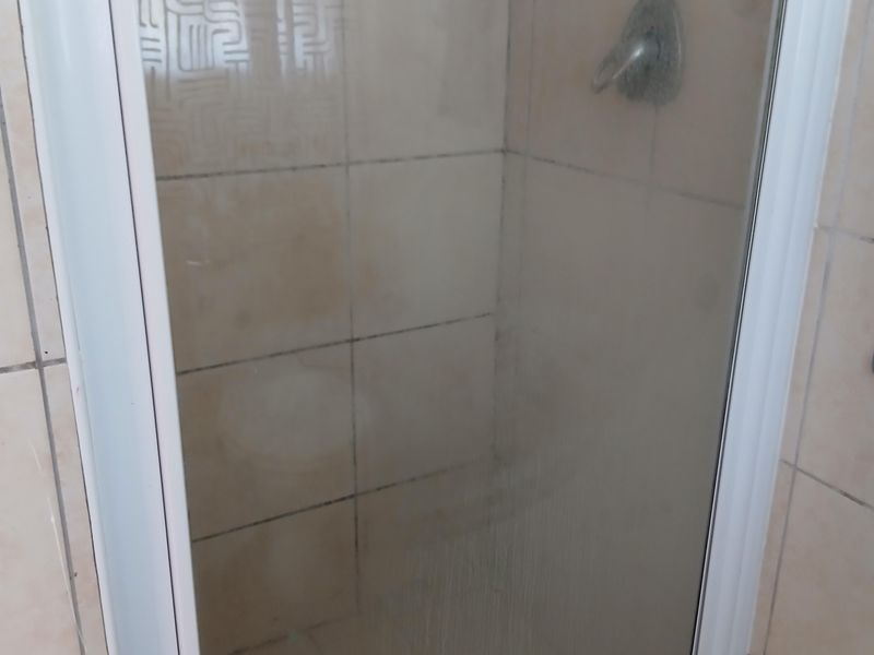A compact shower stall featuring a glass enclosure and tiled walls, currently showing signs of wear and requiring maintenance to the grout and seals.
