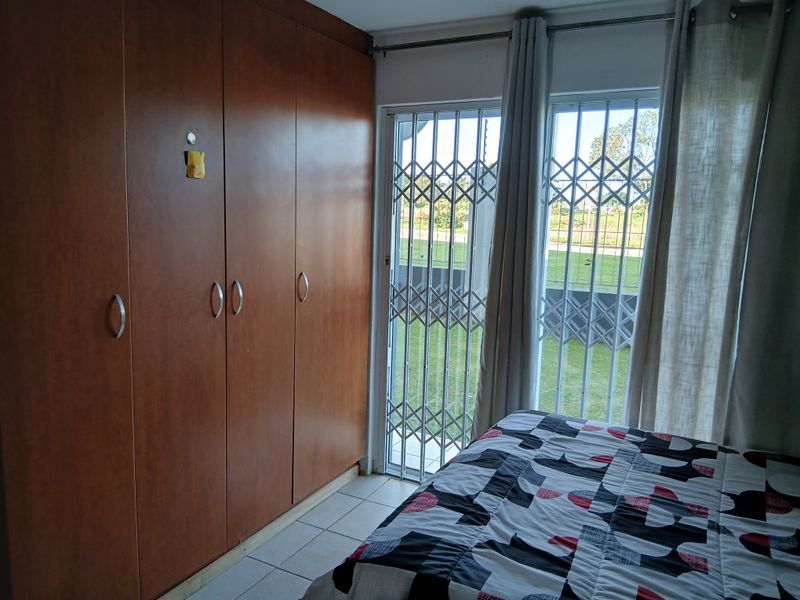 A bedroom featuring built-in wooden cupboards, tiled flooring, and a security gate providing access to the exterior.
