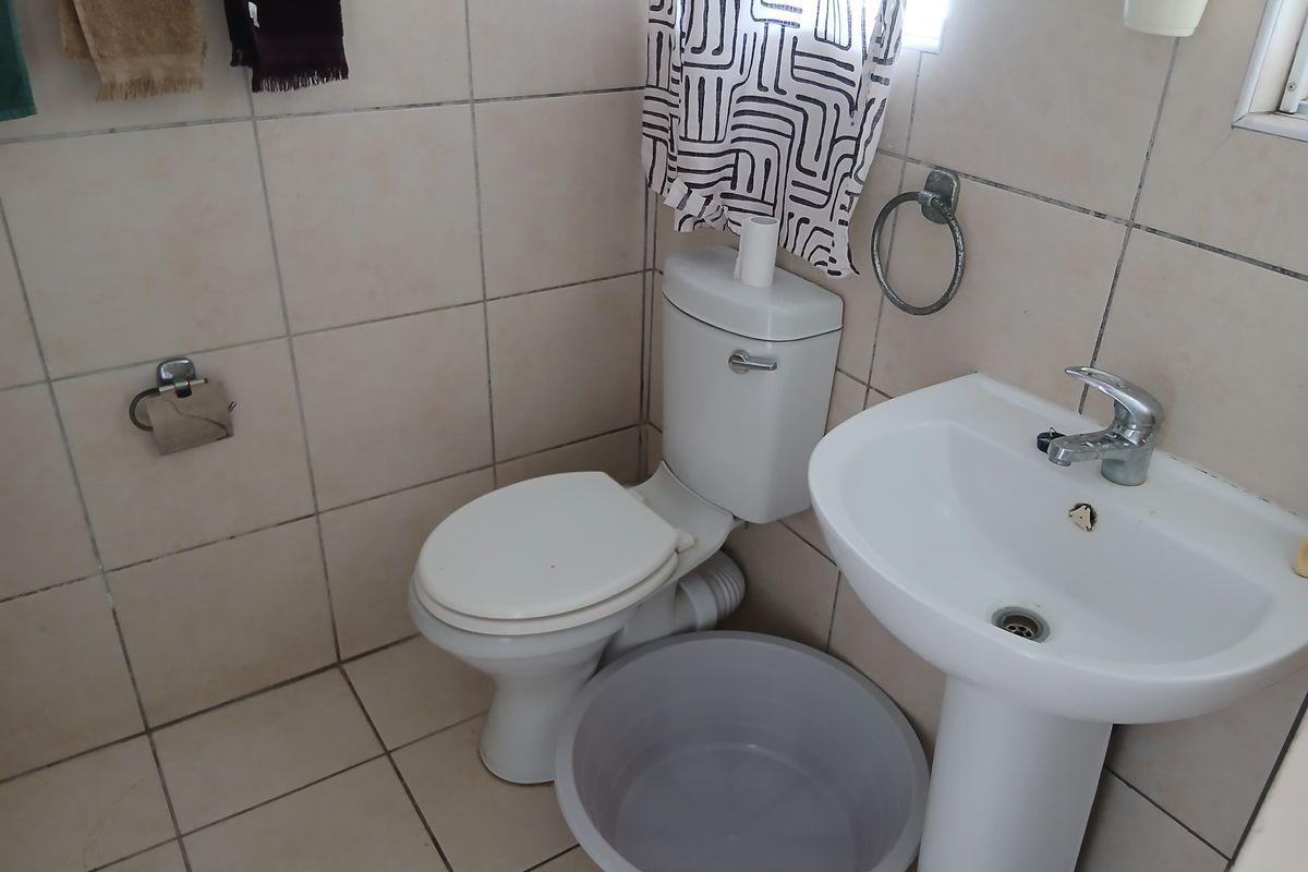 A compact bathroom featuring a pedestal washbasin and toilet with neutral ceramic wall and floor tiling.