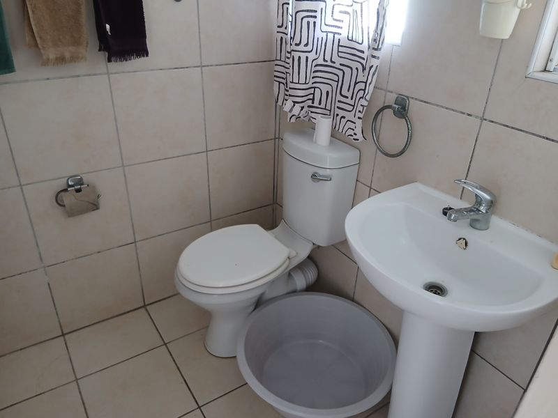 A compact bathroom featuring a pedestal washbasin and toilet with neutral ceramic wall and floor tiling.