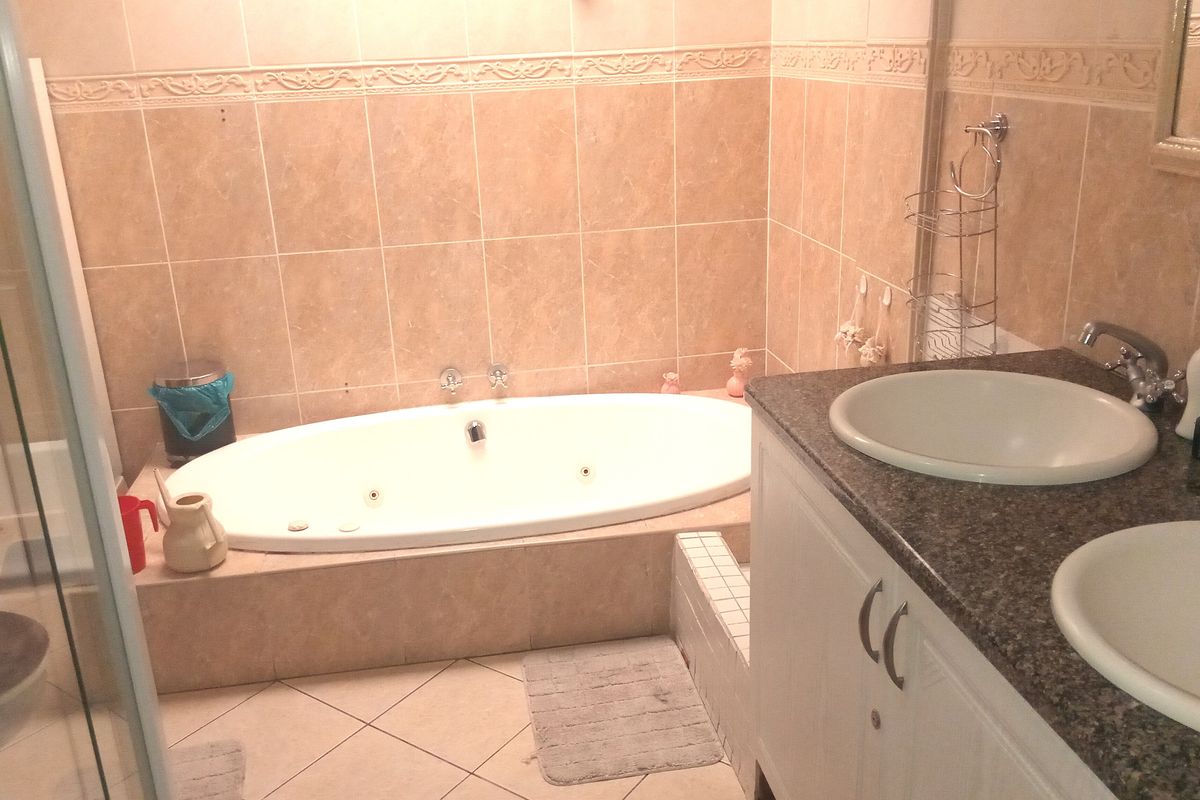 A functional bathroom featuring a built-in jetted bathtub, a double vanity with granite countertops, and a separate glass-enclosed shower area.