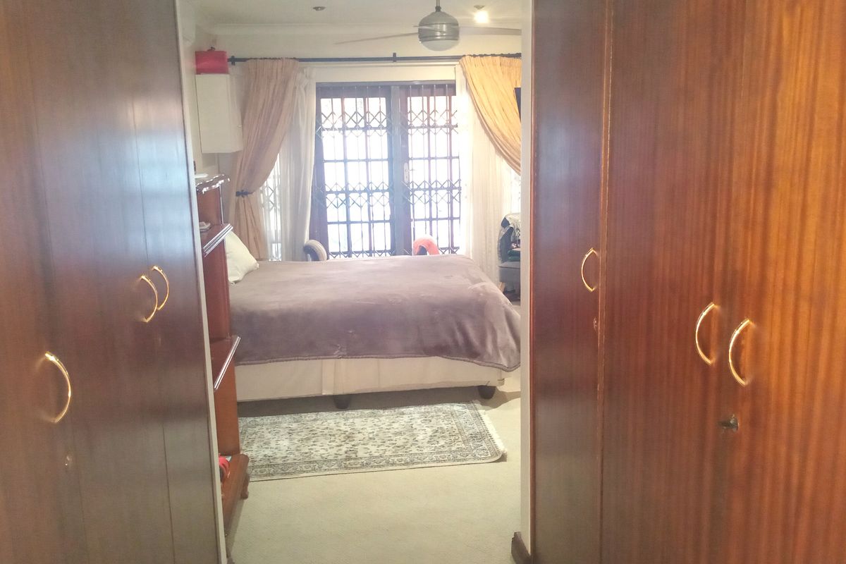 Bedroom featuring built-in wooden cupboards, a ceiling fan, and a sliding door with security gate leading to the exterior.