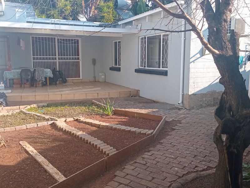 Rear exterior view featuring a covered patio with tiled flooring, security gates, and a paved walkway leading through the garden area.