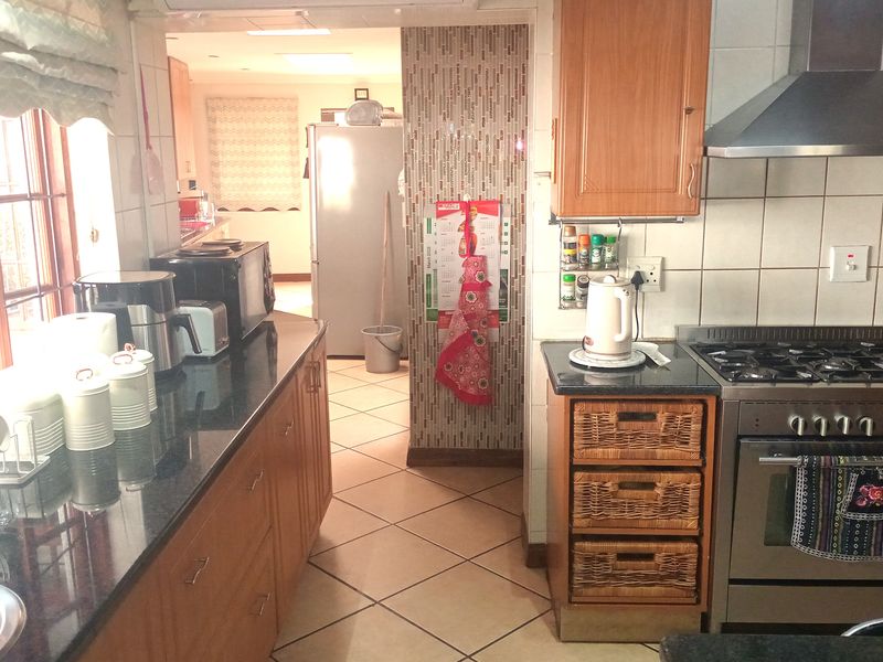 A functional kitchen featuring granite countertops, wooden cabinetry, a gas stove with extractor fan, and tiled flooring, with an adjacent scullery area.