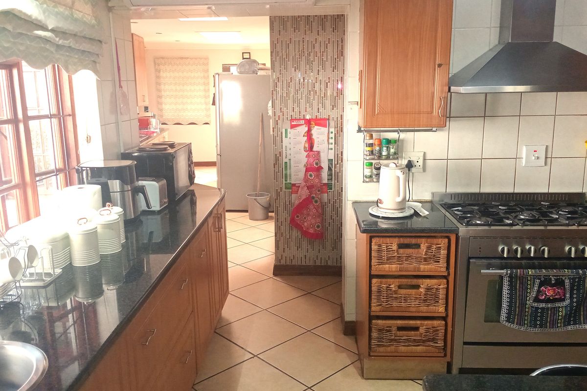 A functional kitchen featuring granite countertops, wooden cabinetry, a gas stove with extractor fan, and tiled flooring, with an adjacent scullery area.