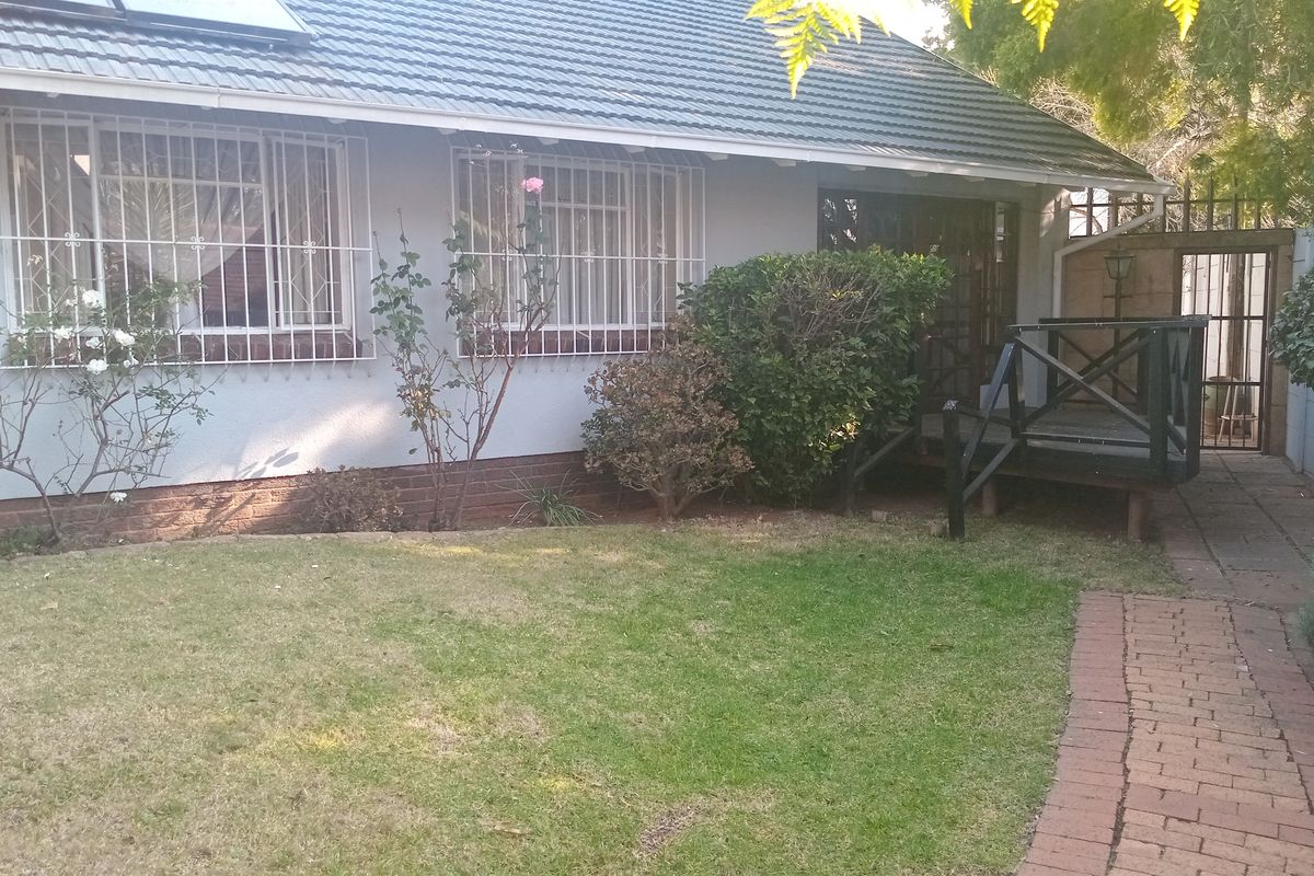 Rear exterior view of the house featuring a small timber deck, brick paved pathway, and security bars on the windows.