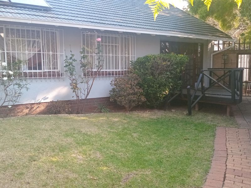 Rear exterior view of the house featuring a small timber deck, brick paved pathway, and security bars on the windows.