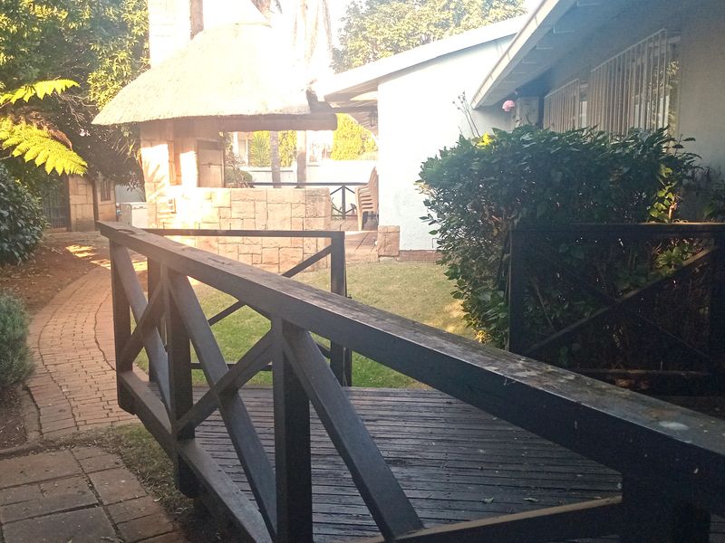 Rear garden area featuring a timber deck, brick pathway, and a thatched lapa with a built-in braai.