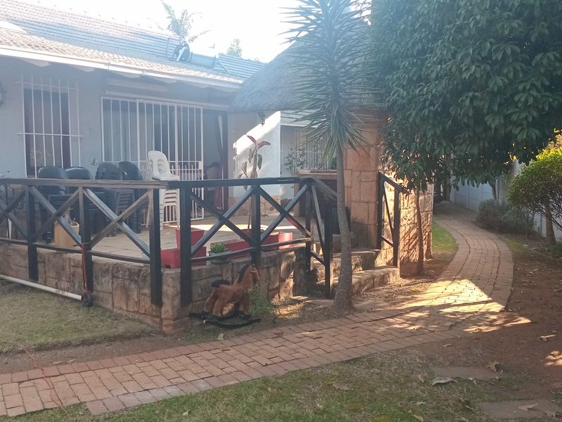 A raised outdoor patio area featuring a timber balustrade and stone cladding, accessible via a brick-paved garden path.