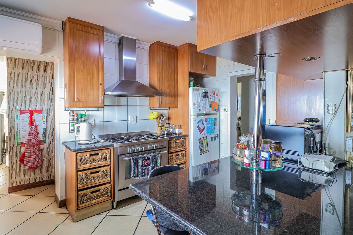 Functional kitchen featuring granite countertops, wooden cabinetry, a gas stove with stainless steel extractor fan, and tiled flooring.
