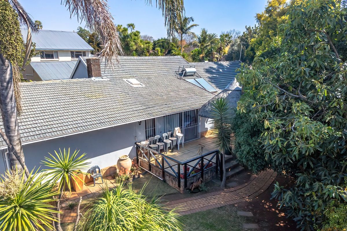 Aerial view of the rear exterior featuring a tiled roof with solar water heating, a paved patio area with timber balustrades, and established garden.