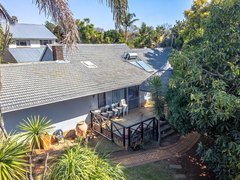 Aerial view of the rear exterior featuring a tiled roof with solar water heating, a paved patio area with timber balustrades, and established garden.