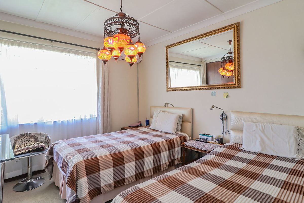A functional bedroom featuring a tiled ceiling, wall-mounted reading lights, and large windows with curtain rails.