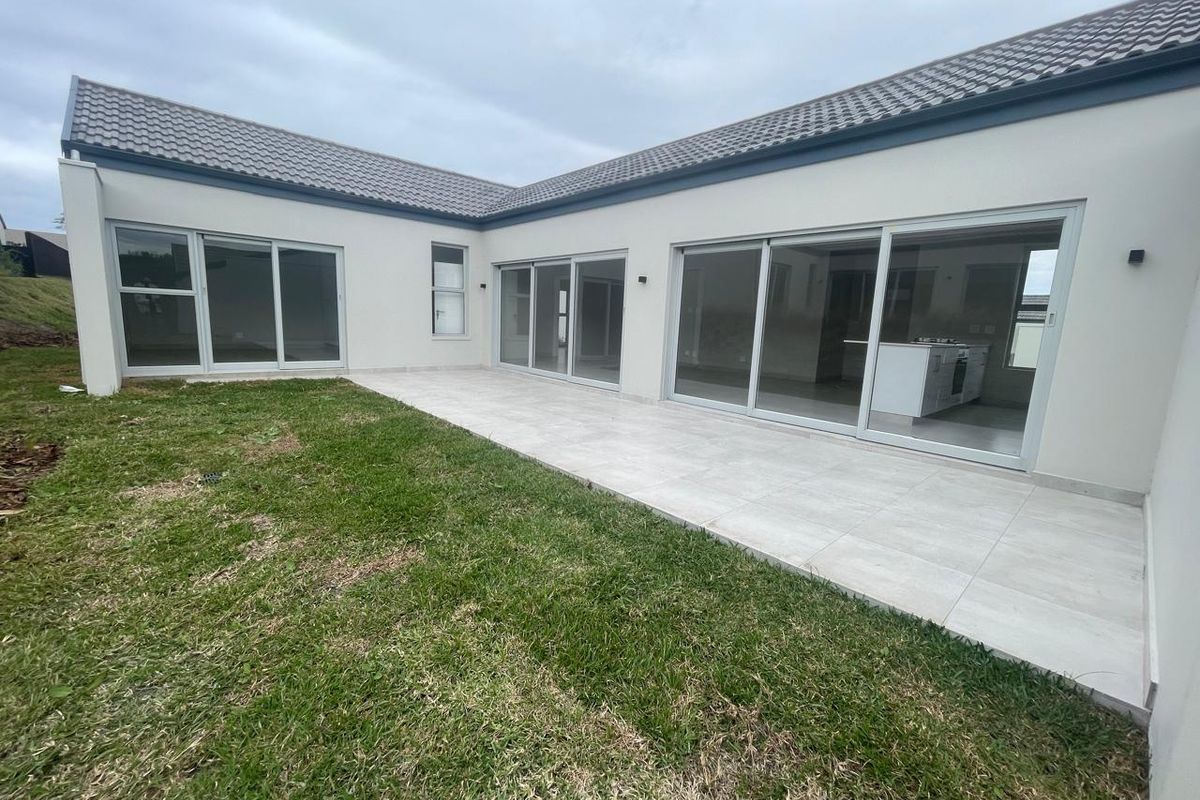 A modern rear exterior view featuring a spacious tiled patio, large sliding glass doors, and a well-maintained lawn area.