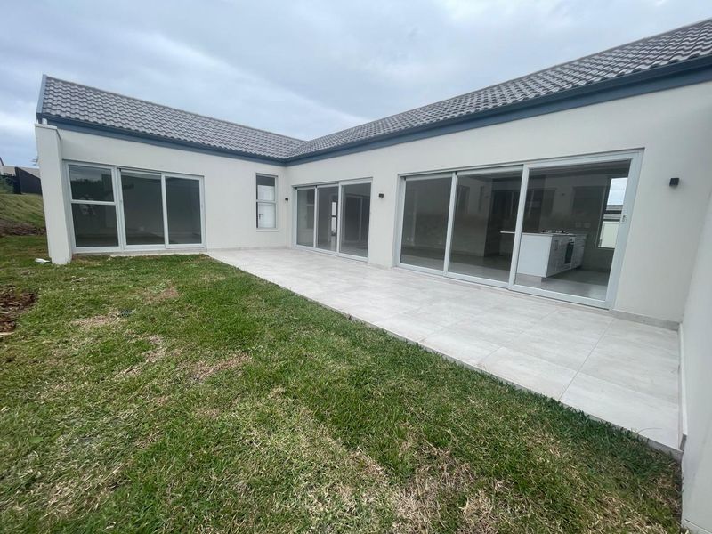 A modern rear exterior view featuring a spacious tiled patio, large sliding glass doors, and a well-maintained lawn area.