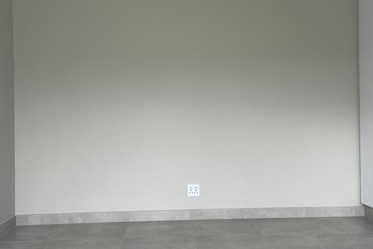A clean, empty bedroom featuring neutral grey tiled flooring, recessed downlights, and a minimalist aesthetic ready for furnishing.