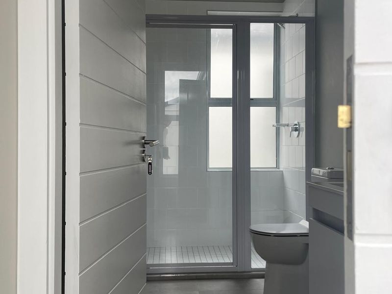A clean, modern bathroom featuring a glass-enclosed shower, contemporary vanity, and neutral floor tiling, viewed through a doorway.