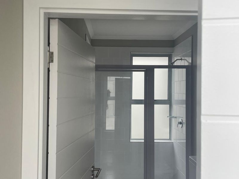 A clean, modern bathroom featuring a glass-enclosed shower, tiled walls, and neutral flooring, viewed through a doorway.
