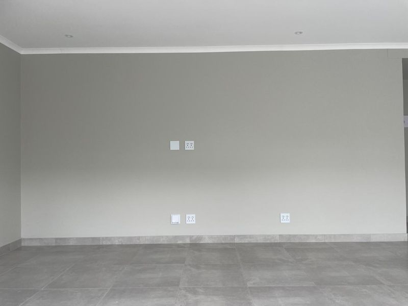 A clean, empty living room featuring neutral grey walls, modern tiled flooring, and recessed downlights, providing a blank canvas for interior design.