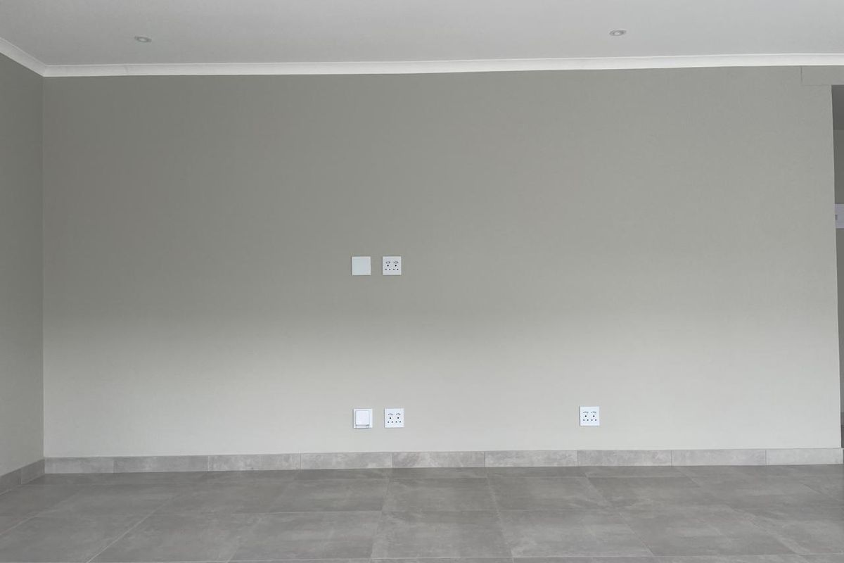 A clean, empty living room featuring neutral grey walls, modern tiled flooring, and recessed downlights, providing a blank canvas for interior design.