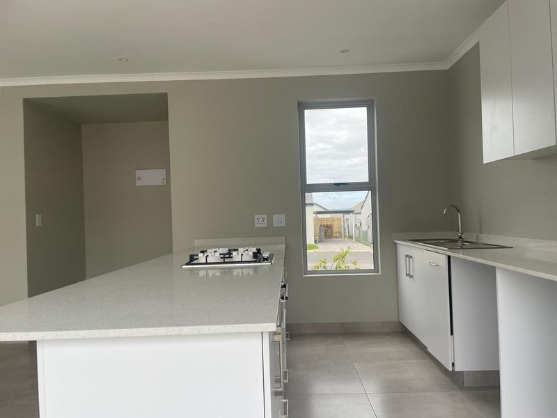 Modern kitchen featuring a central island with a gas hob, quartz countertops, sleek white cabinetry, and tiled flooring in a clean, neutral space.