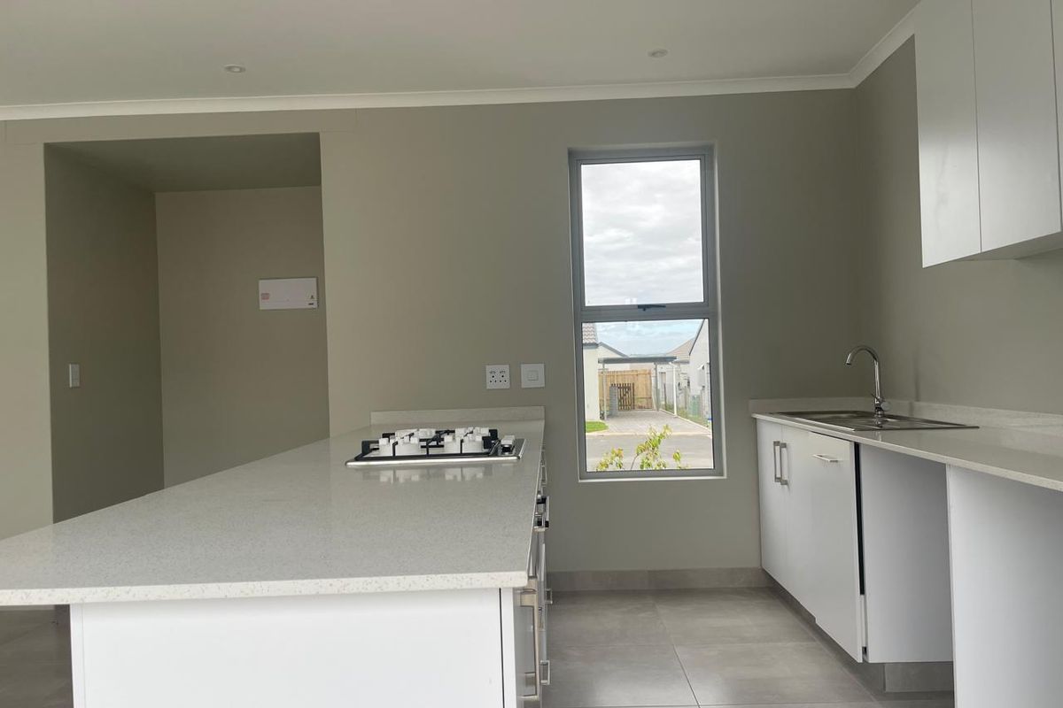 Modern kitchen featuring a central island with a gas hob, quartz countertops, sleek white cabinetry, and tiled flooring in a clean, neutral space.