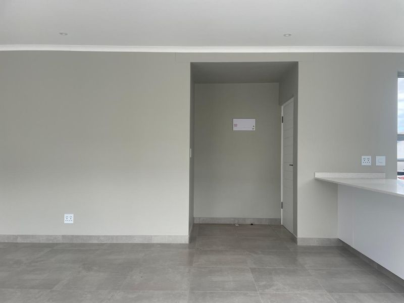 A clean, modern open-plan living space featuring neutral wall tones, large format floor tiles, and a stone-topped breakfast counter.