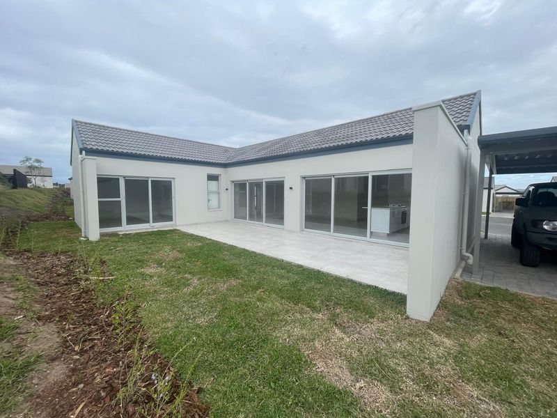 Rear view of a modern house featuring a tiled patio, large sliding glass doors, and an attached carport.