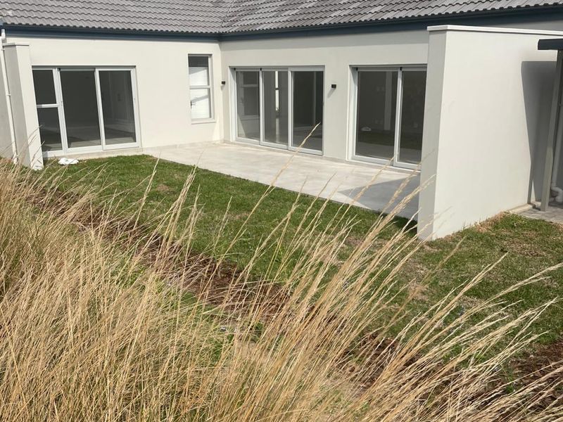 Rear view of the property featuring a paved patio area, lawn, and multiple sliding glass doors providing access to the interior.
