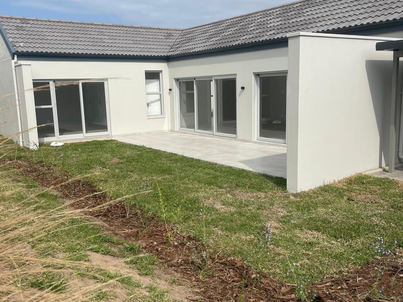 Rear view of the property featuring a tiled patio area, modern sliding glass doors, and a clean plastered facade with a tiled roof.