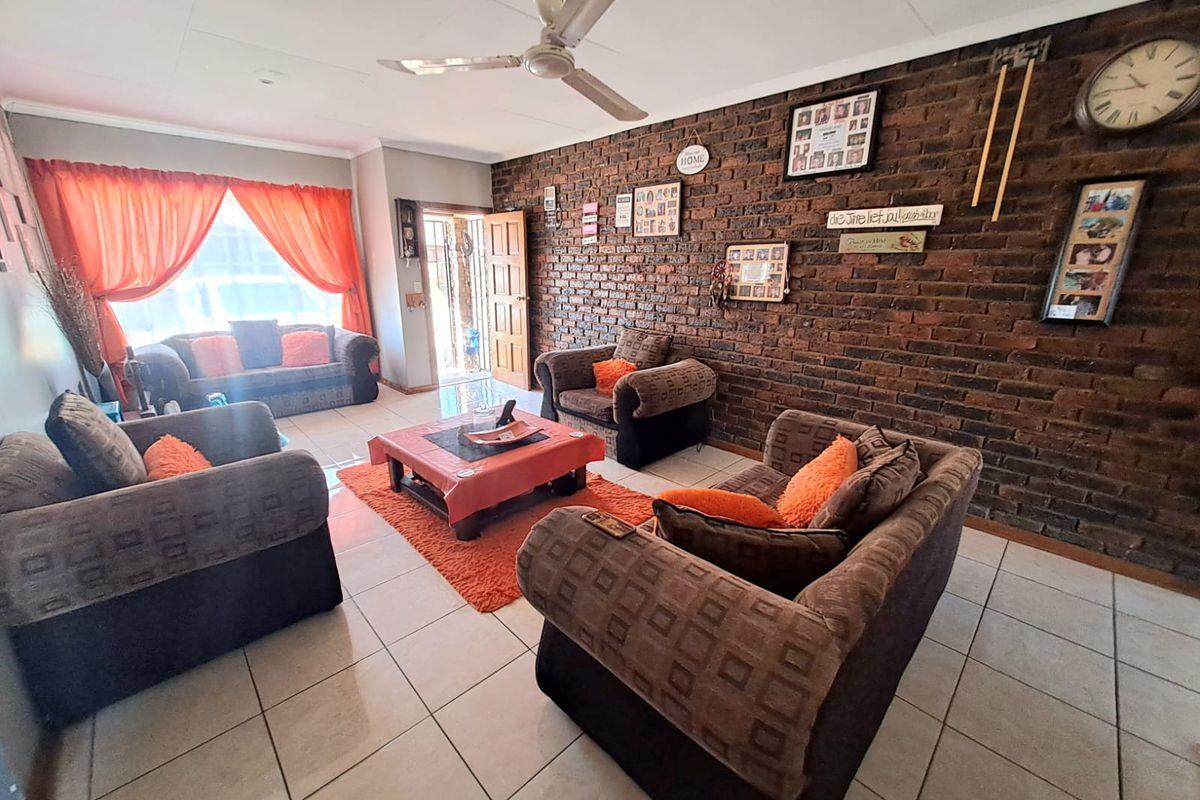 Spacious living room featuring a prominent exposed brick wall, tiled flooring, and a ceiling fan, providing a comfortable and character-filled living space.
