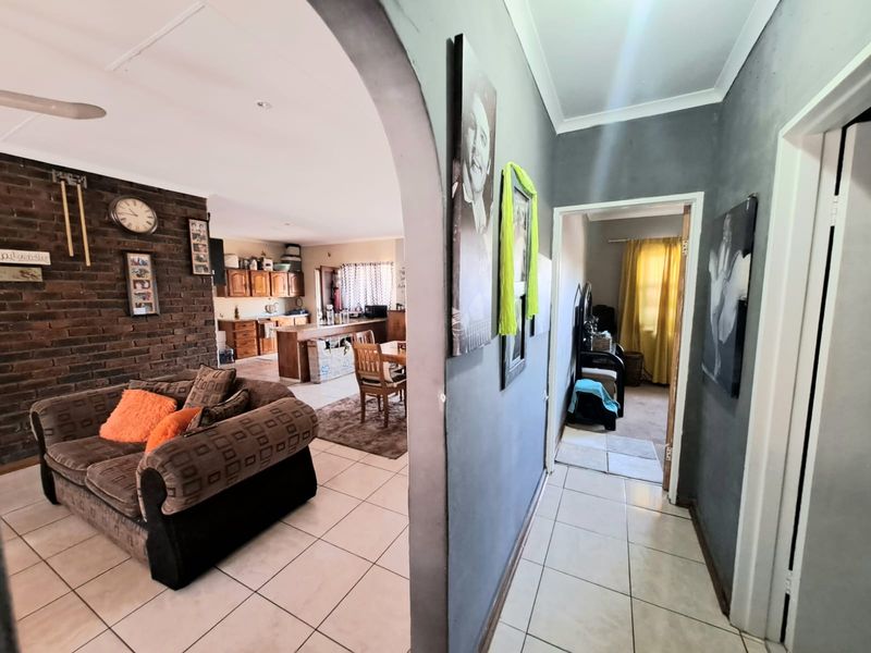 Open plan living area featuring an exposed brick feature wall, ceramic floor tiles, and an arched transition to the kitchen and hallway.