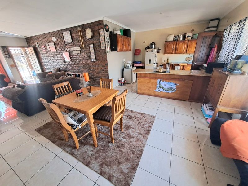Open-plan living and dining area featuring an exposed brick feature wall, tiled flooring, and a functional kitchen with built-in cabinetry and a breakfast bar.