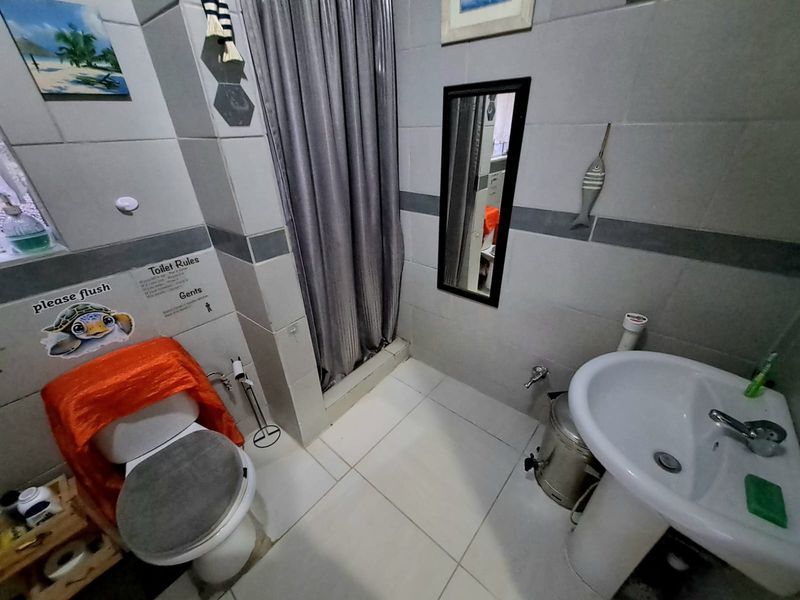 A functional bathroom featuring a pedestal basin, a shower area with a curtain, and neutral ceramic wall and floor tiling.