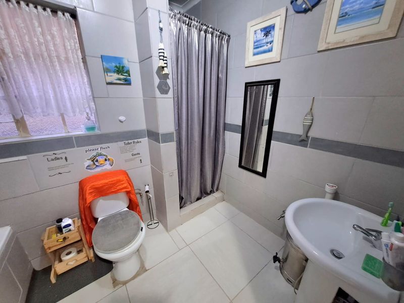A functional bathroom featuring a pedestal basin, toilet, and a shower area with a curtain, finished with neutral wall and floor tiles.