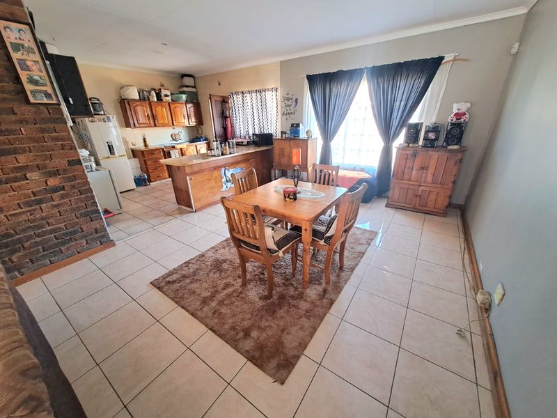 Open-plan living and dining area featuring ceramic floor tiles, an exposed brick wall, and a functional kitchen with wooden cabinetry and a breakfast bar.