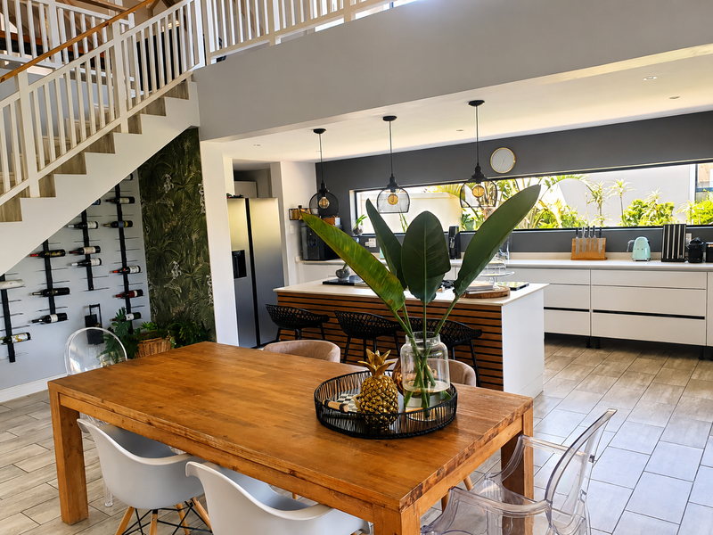 Modern open-plan living area featuring a sleek kitchen with island, dining space, and a striking staircase with integrated wine storage.